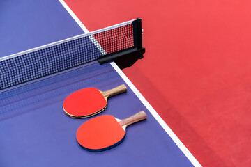 Two pingpong table tennis rackets for playing are laid on next to net on the blue table. This is...