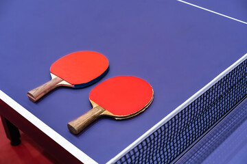 Two pingpong table tennis rackets for playing are laid on next to net on the blue table. This is...