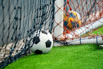 Classical football or soccer ball and goal lying on the artifinal grass. They are ready to play by football player indoor arena.