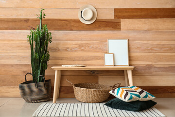 Big cactus, table with frames, basket and pillows near wooden wall
