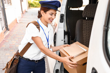 Young postwoman taking box with letters from car