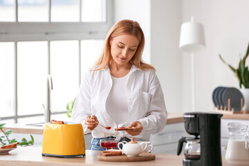 Obraz na płótnie Canvas Mature woman making tasty toasts in kitchen