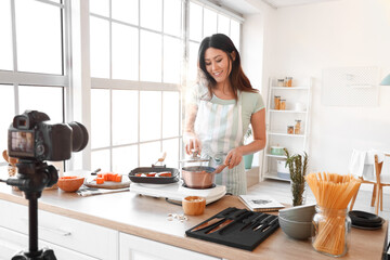 Young Asian woman boiling pumpkin while recording video class in kitchen