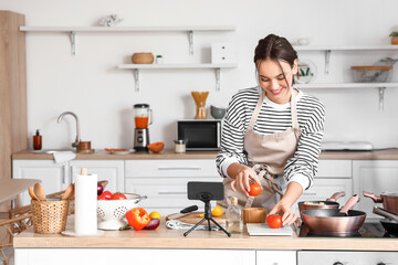 Young woman with fresh tomatoes following cooking video tutorial in kitchen - obrazy, fototapety, plakaty
