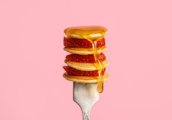 Fork with delicious mini pancakes, strawberry and honey on pink background