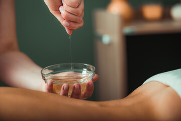 Massage Oil. Therapist pouring aromatic massage oil onto woman’s back