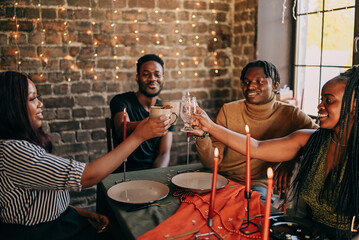 Best friends celebrating new year. Young people with candles, sitting at dining table. Diverse students during christmas party at home, smiling and laughing.