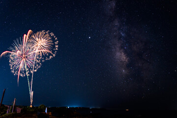 海岸から海の向こうに見える天の川と打ちあがる花火。合成写真