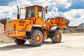 A large front loader transports crushed stone or gravel in a bucket at a construction site or concrete plant. Transportation of bulk materials. Construction equipment. Bulk cargo transportation.