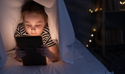 Close up of little girl watching cartoons on the digital tablet at night, copy space