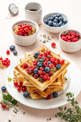 Traditional belgian waffles with fresh berries, raspberries, currant, blueberries, maple syrup, thyme on pink background. Summer concept. Selective focus.