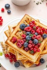 Traditional belgian waffles with fresh berries, raspberries, currant, blueberries, maple syrup, thyme on pink background. Summer concept. Selective focus.