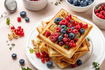 Traditional belgian waffles with fresh berries, raspberries, currant, blueberries, maple syrup, thyme on pink background. Summer concept. Selective focus.