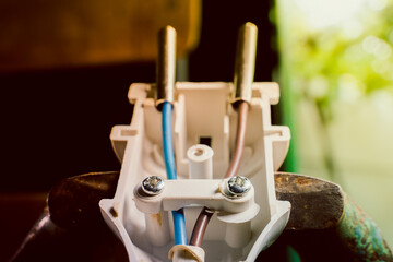 Connecting the wires of an electrical appliance into an electrical plug. A disassembled white plastic electrical plug close-up in an iron vice. Brown and blue wire