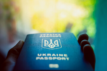 Ukrainian biometric passport in hand close-up on a blurred background. Coat of arms of Ukraine in...