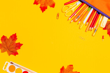 Pencil box with pens on a yellow background with maple leaves. Flat lay. Copy space. Concept of...