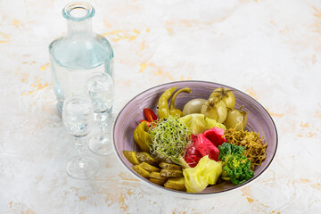 various pickled tomatoes green capers and cabbage in a plate on a white background with vodka
