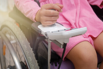 baby girl in a dress sitting on an electric wheelchair indoors. close-up photo of electric wheelchair joystick