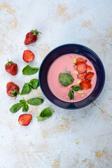 strawberry cream soup with strawberries in a blue plate on a light background with greens vertical photo

