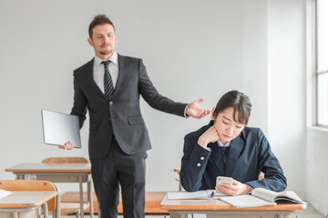 授業中にスマホを使う高校生と注意する先生
