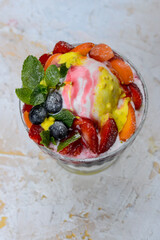 a scoop of ice cream with berries and strawberries in a transparent glass on a white background, vertical photo
