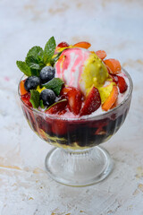 a scoop of ice cream with berries and strawberries in a transparent glass, vertical photo
