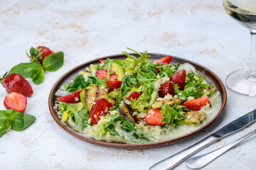 fresh salad with grilled avocado and strawberries and couscous porridge in a clay plate, macro photo
