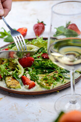fresh salad with grilled avocado and strawberries and couscous porridge in a clay plate with utensils in hand

