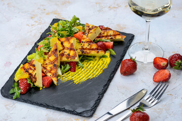 grilled cheese with citrus and salad on a black slate on a white background with a glass of wine
