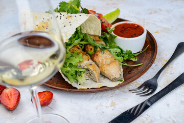 shawarma with chicken in pita bread on a plate with vegetables and pepper on a white background with a glass of wine close-up
