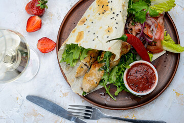 shawarma with chicken in pita bread on a plate with vegetables and pepper on a white background with a glass of wine macro photo
