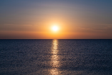Naklejka na ściany i meble Beautiful Sunset with large yellow sun over mediterranean sea. Deep blue water and orange sky.