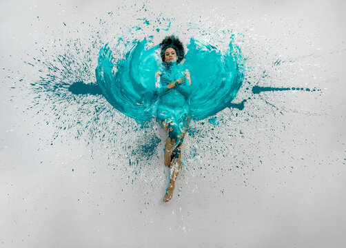 expressive sexy woman lies naked elegant on the floor in turquoise blue color abstract painted bodypainting woman on the splashed ground, spreads the paint in form of angel wings