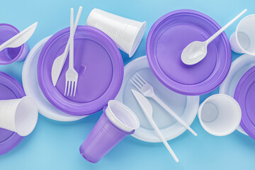 A set of disposable, lilac and white, plastic utensils. Blue background, copy space. The concept of ecology and recycling of plastic waste