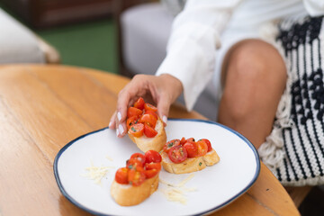 Close shot of a dish with bruschettas with tomatoes in a summer cafe, a girl in an elegant dress takes a bruschetta