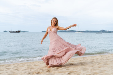 Fototapeta na wymiar Beautiful young blonde woman in a long pink dress on the beach, tender, posing, the wind develops the dress hair, romantic, free