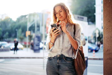 Handsome young smiling woman with mobile phone walking on the street