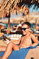  Happy  boy in Sunglasses Lying on a sunbed on the beach. Handsome  happy boy having fun .Summer vacation sea sun tan vegeterian food concept