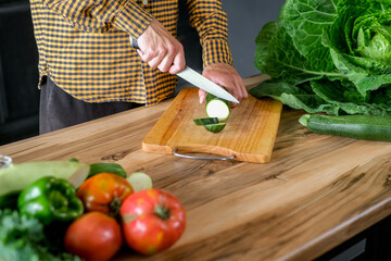 Cook holds knife in hand and cuts on cutting board green zucchini for salad or fresh healthy...
