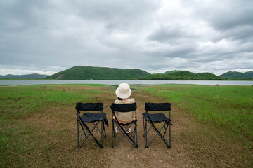 The young woman sits on the camping chair and looks at the view of the reservoir at the Huai Phak...