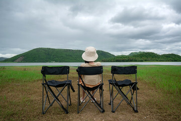 The young woman sits on the camping chair and looks at the view of the reservoir at the Huai Phak...