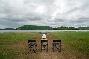 The young woman sits on the camping chair and looks at the view of the reservoir at the Huai Phak Reservoir, Tha Yang District, Phetchaburi, Thailand.