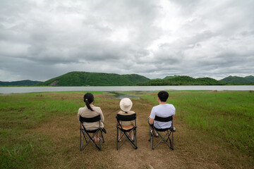 The mother, daughter, and father sit on the camping chair and look at the view of the reservoir at the Huai Phak Reservoir, Tha Yang District, Phetchaburi, Thailand.