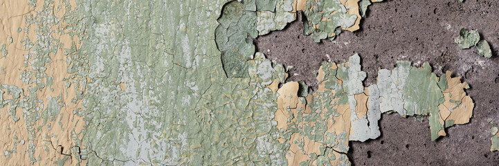 Peeling paint on the wall. Panorama of a concrete wall with old cracked flaking paint. Weathered rough painted surface with patterns of cracks and peeling. Wide panoramic grunge texture for background