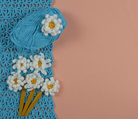 Crocheted daisies flowers, hooks, and a thread skein on blue crochet and pink textile background.