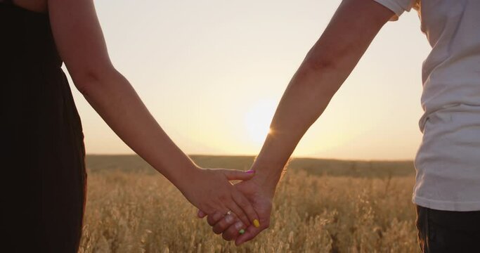Couple in love holding hands against the background of the sun. Close up