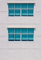 Two rows of glass windows on large square concrete tiles wall of office building in vertical frame