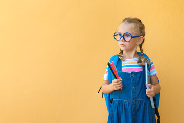 serious pensive face smart schoolgirl child in glasses in school uniform holds colored pencils,...