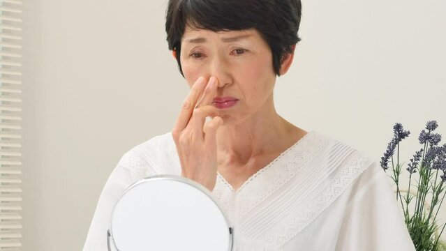 リビングで鏡で顔を見て悩むシニア女性