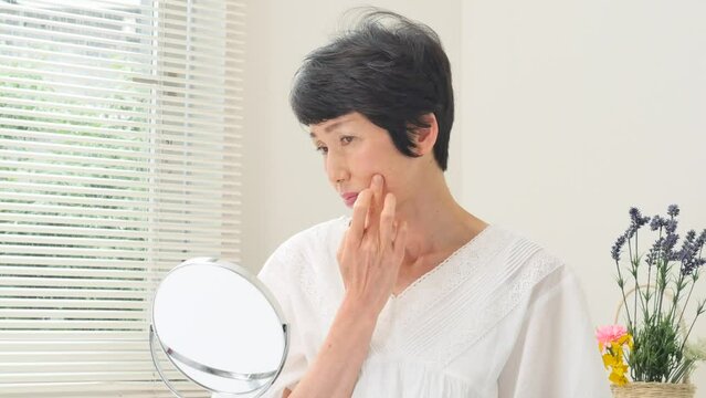 リビングで鏡で顔を見て悩むシニア女性
